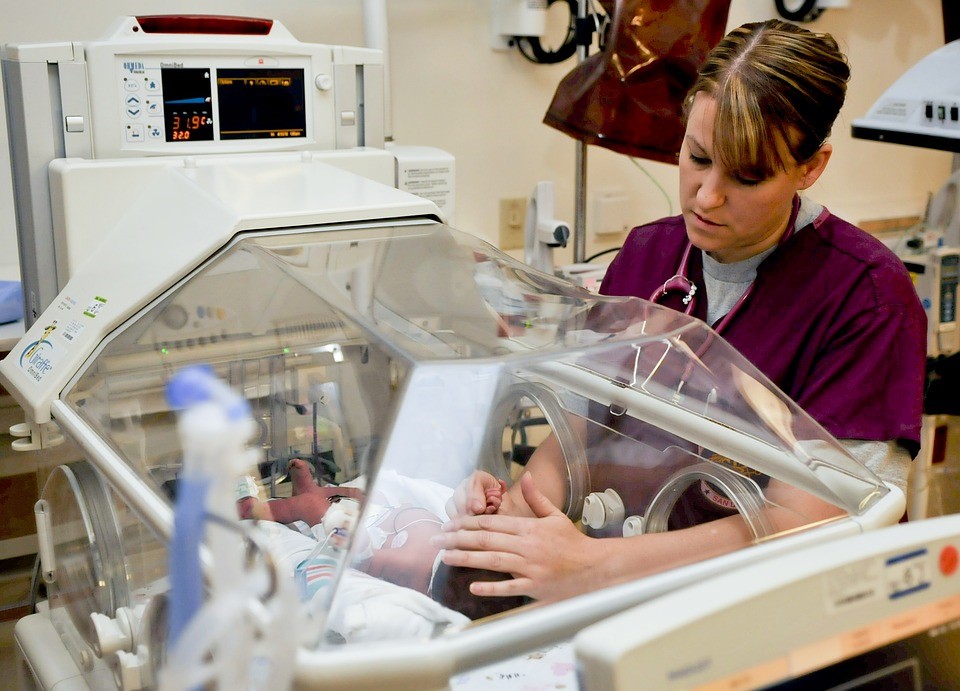 A Nurse Reaching Inside an Incubator to Examine a Newborn Baby